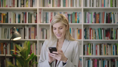 portrait-of-stylish-blonde-business-woman-smiling-enjoying-texting-browsing-online-using-smartphone-social-media-app-wearing-suit-in-library-office