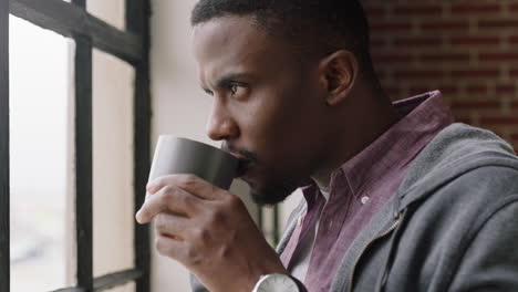 Porträt-Eines-Jungen-Afroamerikanischen-Mannes,-Der-Zu-Hause-Kaffee-Trinkt-Und-Einen-Entspannten-Morgen-Genießt,-Der-Aus-Dem-Fenster-Blickt-Und-Vorausschauend-Denkt,-Dass-Ein-Erfolgreicher-Mann-Sich-Aus-Nächster-Nähe-Entspannt