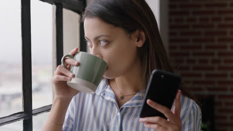 Schöne-Hispanische-Frau,-Die-Zu-Hause-Kaffee-Trinkt-Und-Ihr-Smartphone-Nutzt,-Genießt-Entspannten-Morgen-Das-Durchsuchen-Von-Nachrichten-Und-Schaut-Aus-Dem-Fenster,-Um-Im-Voraus-Zu-Planen,-SMS-über-Mobiltelefonnetzwerke-Zu-Schreiben