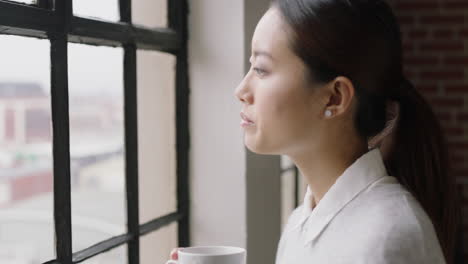 Porträt-Einer-Schönen-Asiatischen-Frau,-Die-Zu-Hause-Kaffee-Trinkt,-Glücklich-Lächelt-Und-Einen-Erfolgreichen-Lebensstil-Genießt,-Der-Aus-Dem-Fenster-Blickt-Und-Die-Zukunft-Plant-Und-Sich-In-Einem-Gemütlichen-Apartment-Loft-Entspannt