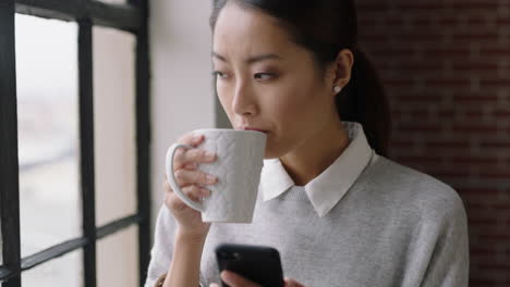Schöne-Asiatische-Geschäftsfrau,-Die-Zu-Hause-Kaffee-Trinkt-Und-Ihr-Smartphone-Nutzt,-Genießt-Entspannten-Morgen-Das-Durchsuchen-Von-Nachrichten-Und-Schaut-Aus-Dem-Fenster.-Sie-Plant-Vorausschauende-Textnachrichten-über-Mobiltelefonnetzwerke