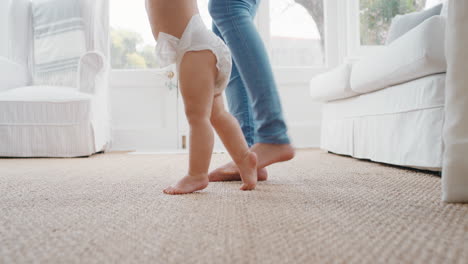 baby-taking-first-steps-toddler-learning-to-walk-with-mother-gently-helping-infant-teaching-child-at-home-motherhood-trust
