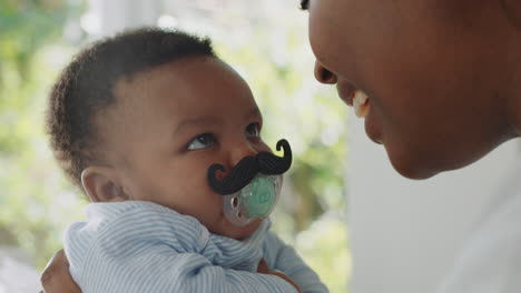 funny-baby-with-moustache-pacifier-happy-mother-having-fun-with-toddler-at-home-enjoying-silly-humor-with-child-sucking-on-dummy