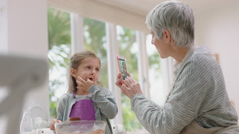 Glückliche-Großmutter-Fotografiert-Mit-Dem-Smartphone-Die-Süße-Enkelin-In-Der-Küche-Und-Mischt-Zutaten-Zum-Backen,-Schmeckt-Schokoladensoße.-Oma-Teilt-Ihr-Wochenende-Mit-Ihrem-Enkelkind-In-Den-Sozialen-Medien