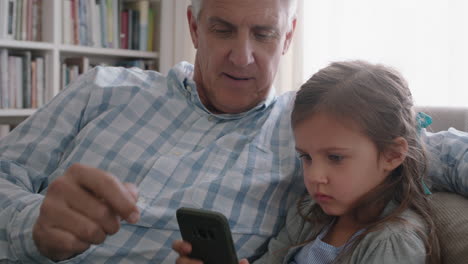 Glücklicher-Großvater-Zeigt-Kleinem-Mädchen,-Wie-Man-Das-Smartphone-Benutzt,-Und-Lehrt-Neugierige-Enkelin-Moderne-Technologie.-Intelligentes-Kind-Lernt-Mobiltelefon,-Das-Mit-Opa-Auf-Dem-Sofa-Sitzt