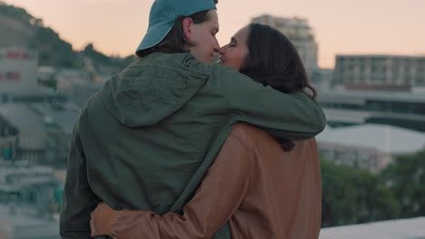 young-caucasian-couple-kissing-on-rooftop-embracing-romance-sharing-intimate-connection-hanging-out-enjoying-view-of-city-at-sunset