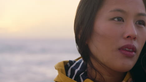 portrait-of-happy-asian-woman-enjoying-peaceful-contemplation-exploring-carefree-lifestyle-relaxing-on-beach-feeling-positive-at-sunrise