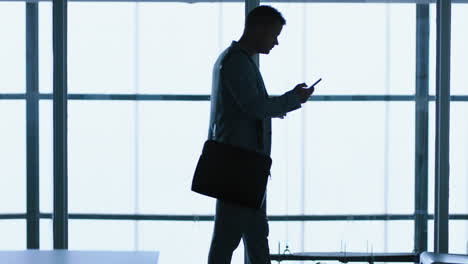 silhouette-businessman-using-smartphone-texting-browsing-messages-on-mobile-phone-sending-email-communication-drinking-coffee-waiting-in-office-4k