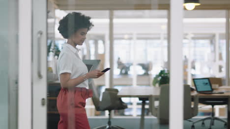 mixed-race-business-woman-using-smartphone-walking-through-office-texting-sending-emails-successful-female-executive-checking-messages-on-mobile-phone-arriving-at-busy-workplace-4k