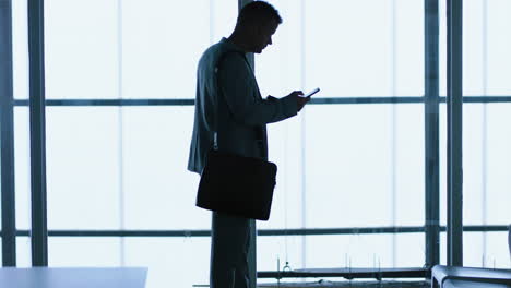 Silhouette-Eines-Geschäftsmannes,-Der-Sein-Smartphone-Nutzt,-Um-SMS-Zu-Schreiben,-Nachrichten-Auf-Dem-Mobiltelefon-Zu-Durchsuchen-Und-E-Mails-Zu-Senden,-Kommunikation-Zu-Vernetzen-Und-Online-Im-Büro-Zu-Warten,-4k