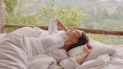 beautiful-woman-waking-up-in-bed-at-hotel-resort-enjoying-vacation-in-paradise-4k