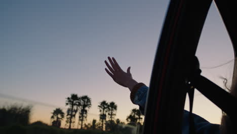 woman-in-car-holding-hand-out-window-feeling-wind-blowing-through-fingers-driving-in-countryside-travelling-on-summer-vacation-road-trip-enjoying-freedom-on-the-road-at-sunset