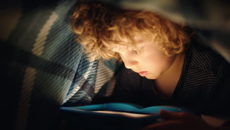 Fröhlicher-Kleiner-Junge,-Der-Unter-Einer-Decke-Einen-Digitalen-Tablet-Computer-Benutzt-Und-Spaß-Daran-Hat,-Auf-Der-Touchscreen-Technologie-Zu-Lernen,-Spiele-Zu-Spielen-Und-Vor-Dem-Schlafengehen-Spaß-Zu-Haben