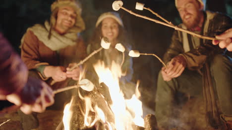 group-of-friends-sitting-by-campfire-roasting-marshmallows-chatting-sharing-stories-camping-in-forest-at-night-enjoying-outdoor-adventure