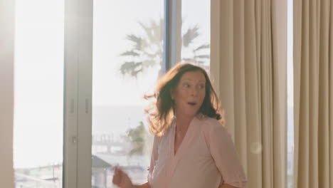 happy-woman-dancing-in-hotel-room-having-fun-enjoying-successful-travel-vacation-healthy-middle-aged-female-celebrating-retirement-at-sunrise