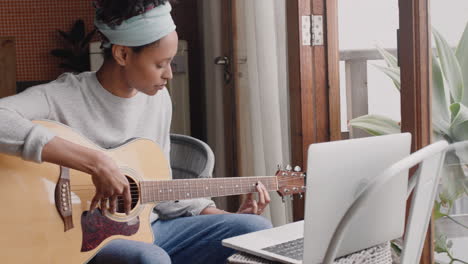 Mujer-Joven-Tocando-La-Guitarra-En-Casa-Aspirante-A-Músico-Aprendiendo-A-Tocar-Instrumentos-Musicales-Usando-Una-Computadora-Portátil-Disfrutando-De-La-Expresión-Creativa-Practicando-Música