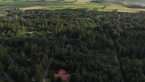 Aerial-panoramic-footage-of-landscape.-Buildings-between-trees-in-forest,-fields-and-pastures.-Wind-farm-in-distance.-Denmark