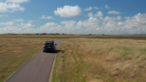 Family-car-driving-on-narrow-road-in-countryside.-Meadows-and-pastures-with-high-grass-along-pathway.-Denmark