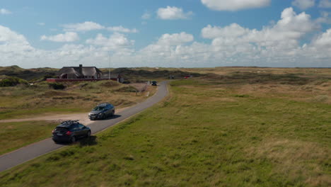 Car-driving-on-narrow-road-and-passing-by-another-vehicle-and-building.-Panoramic-view-of-flat-landscape.-Denmark