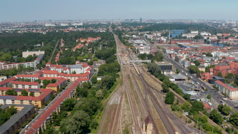Tilt-down-footage-of-straight-railway-line-leading-through-urban-neighbourhood.-Aerial-view-of-traffic-on-track,-passing-trains.-Berlin,-Germany