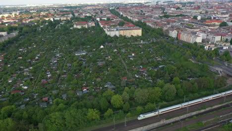 Aerial-view-of-express-train-driving-along-block-of-community-gardens-in-city.-Calm-and-quiet-residential-district.-Berlin,-Germany