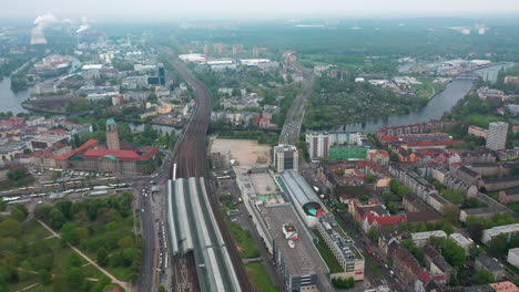 Aerial-panoramic-shot-of-town.-Traffic-on-roads-in-residential-borough-around--train-station.-Industrial-area-with-smoking-factory-chimneys-in-background.-Berlin,-Germany