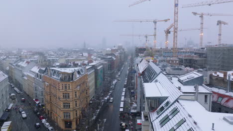 Aerial-view-of-city-streets-in-winter.-Fly-around-construction-site-with-group-of-tower-cranes.-Snowfall-limiting-visibility.-Berlin,-Germany