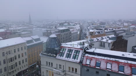 Slide-and-pan-footage-of-rooftop-glass-cupola-on-corner-house-in-town.-Snowing-in-urban-neighbourhood.-Construction-cranes-in-background.-Berlin,-Germany