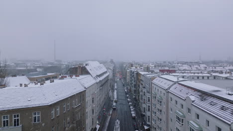 Elevated-footage-of-buildings-along-street-in-urban-neighbourhood.-Winter-in-city,-snowfall-limiting-visibility.-Berlin,-Germany