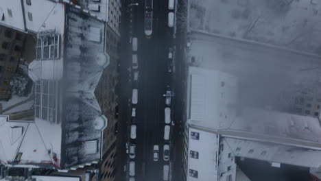 Aerial-birds-eye-overhead-top-down-panning-view-on-car-driving-on-street-in-winter-town.-Snowed-roofs-of-buildings-around.-Berlin,-Germany