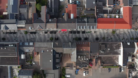 Top-down-view-of-Torvegade-in-Esbjerg,-one-of-Denmark's-longest-pedestrian-avenue.-Overhead-flight-sliding-with-pedestrian-strolling-downtown-and-car-parked-parking-lot