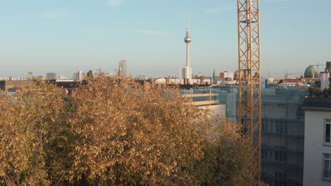 Rise-up-reveal-footage-of-cityscape-behind-tree.-Roofs-of-urban-neighbourhood-and-fernsehturm,-tall-TV-lookout-tower.-Berlin,-Germany.