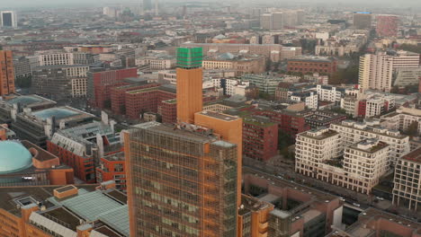 Slide-and-pan-footage-of-top-of-modern-business-building-towering-above-development-in-town.-Berlin,-Germany
