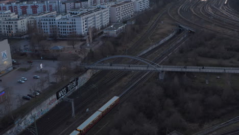 Aerial-view-of-a-passenger-train-passing-by-from-city-and-trees-in-Berlin,-Germany-surrounded-by-residential-house-during-an-early-morning
