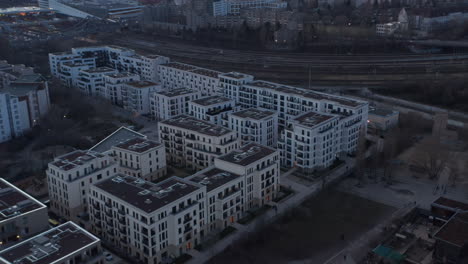 Aerial-circular-motion-view-of-empty-rooftop-of-residential-houses-besides-railway-line-with-people-walking-and-running-outside-building-in-lane-during-cloudy-sky-morning-in-Berlin,-Germany