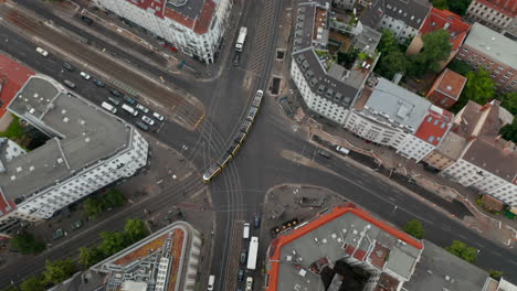 Aerial-view-of-tram-passes-through-intersection-on-Rosenthaler-Platz.-Tilt-up-reveal-cityscape-with-Fernsehturm-TV-tower.-Berlin,-Germany.
