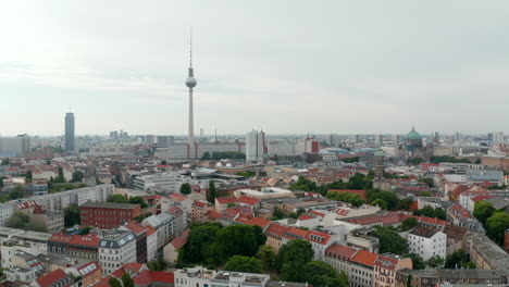 Aerial-view-of-city-centre,-descending-footage-of-town-skyline-with-tall-Fernsehturm-TV-tower.-Overcast-sky.-Berlin,-Germany.