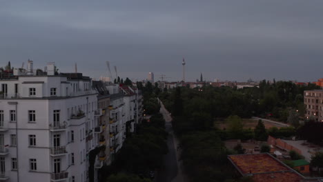 Forwards-fly-above-public-park-in-urban-neighbourhood-in-morning-before-sunrise.-Fernsehturm-TV-tower-in-distance.-Berlin,-Germany