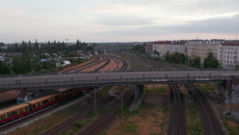 Tracking-of-Sbahn-train-arriving-into-train-station-under-Bosebrucke-bridge.-Aerial-view-of-multitrack-railway-line.-Berlin,-Germany