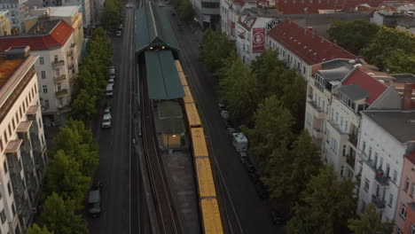 Aerial-view-of-train-driving-in-town-street.-Forwards-tracking-of-yellow-Sbahn-unit.-Buildings-lit-by-bright-morning-sun.-Berlin,-Germany