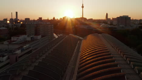 AERIAL:-Flight-over-Berlin,-Germany-Ostbahnhof-Central-Train-Station-at-beautiful-Sunset,-Sunlight-and-view-on-Alexanderplatz-TV-Tower,-Sunflairs