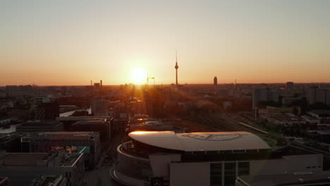 Berlin,-Germany-at-beautiful-Sunset,-Sunlight-Golden-Hour-and-view-over-Alexanderplatz-TV-Tower-and-Mercedes-Benz-Arena-with-flashing-advertisements-,Sunflairs-above-Rooftops-in-2019