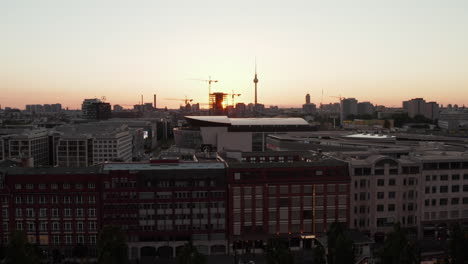 AERIAL:-Flight-over-Berlin,-Germany-at-beautiful-Sunset,-Sunlight-and-view-on-Alexanderplatz-TV-Tower-and-Ostbahnhof,-Sunflairs