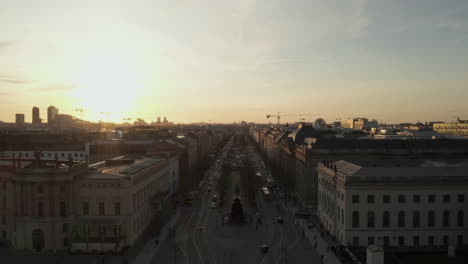 AERIAL:-Scenic-low-flight-through-busy-Berlin,-Germany-Street-towards-Brandenburg-Gate-in-beautiful-epic-sunset-light