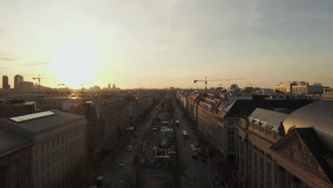 AERIAL:-Spectacular-low-flight-through-busy-Berlin,-Germany-Street-towards-Brandenburg-Gate-in-beautiful-golden-sunset-light