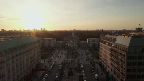 AERIAL:-Scenic-low-flight-through-busy-Berlin,-Germany-Street-towards-Brandenburg-Gate-in-beautiful-golden-sunset-light
