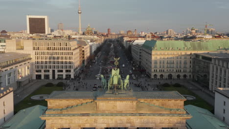 AERIAL:-Slowly-approaching-Brandenburg-Gate-and-Tiergarten-in-beautiful-sunset-sunlight-with-close-view-on-Quadriga-Green-Statue-in-Berlin,-Germany