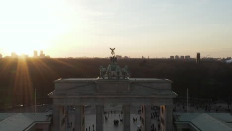 AERIAL:-Slowly-approaching-Brandenburg-Gate-and-Tiergarten-in-beautiful-sunset-sunlight-with-close-view-on-Quadriga-Green-Statue-in-Berlin,-Germany