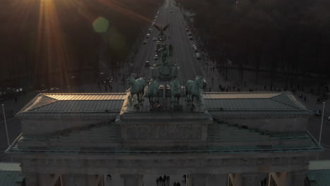 AERIAL:-Slowly-approaching-Brandenburg-Gate-in-beautiful-sunset-sunlight-and-tilting-down-on-Quadriga-Green-Statue-in-Berlin,-Germany