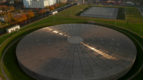 Arquitectura-Moderna-De-Edificios-Planos-Futuristas,-Arena-De-Velódromo-En-Berlín,-Alemania-Con-Reflejo-Del-Sol-En-El-Techo-De-Metal,-Vista-Aérea-Inclinada-Hacia-Abajo